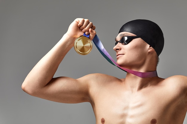 Пловец с медалью на сером фоне радуется победе, спортсмен в отличной физической форме празднует победу, сжимая в руке медаль, концепция победы, серый фон, пространство для копирования