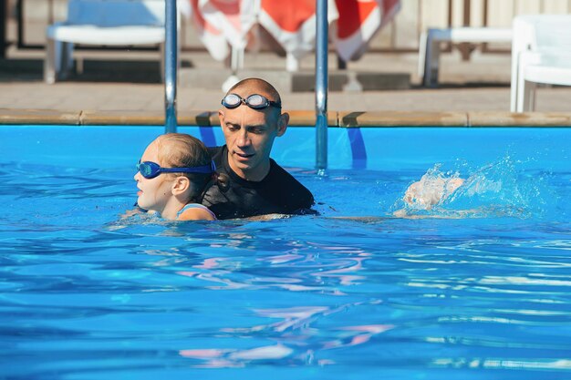 Swimming coach conducts an individual lesson with an 8-year-old\
girl in the water of the pool