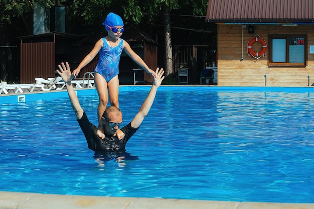 The swimming coach conducts an individual lesson with the girl\
in the outdoor pool