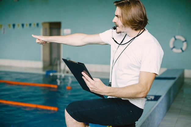 Swimming coach standing by the pool. Checking swimming records. Holding clipboard.