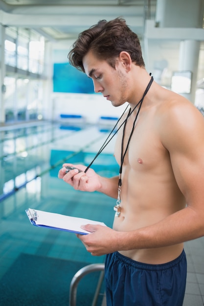 Foto istruttore di nuoto che tiene cronometro e appunti in piscina