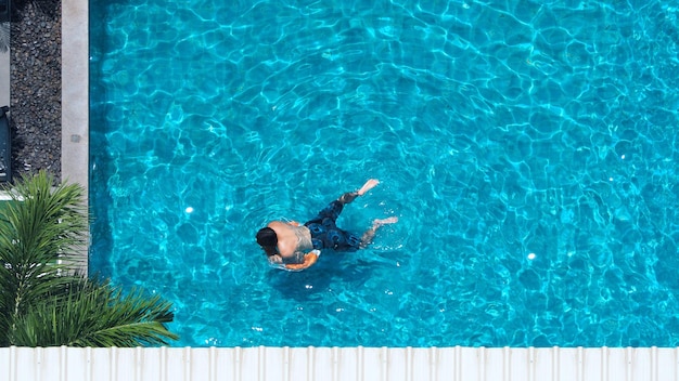 Бассейн голубого цвета с чистой водой и людьми, наслаждающимися летним солнечным днем и углом обзора сверху