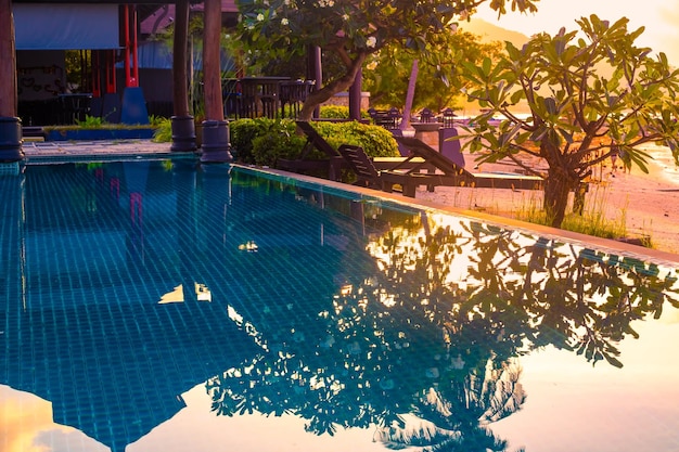 Swimming pool by the sea with plumeria reflection in the water at sunset Rest and relaxation