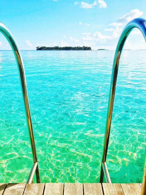 Swimming pool rails by sea against blue sky