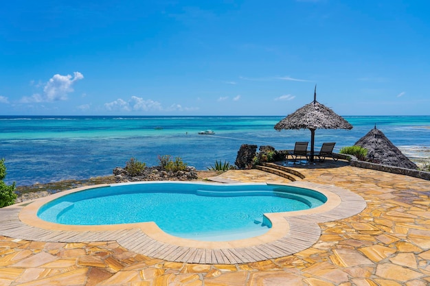 Swimming pool and straw umbrella on a tropical beach near the sea in sunny day on the island of Zanzibar Tanzania East Africa