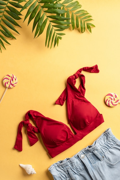 Photo swimsuit, denim shorts and palm leaves on a yellow background. beach travel concept. vertical image. copy space