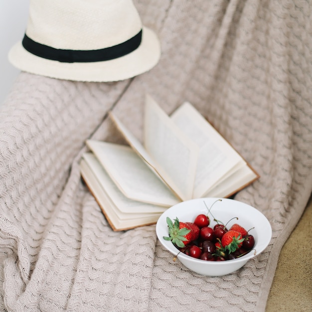 Swimsuit hat book and fresh sweet cherries and strawberries on wooden surface