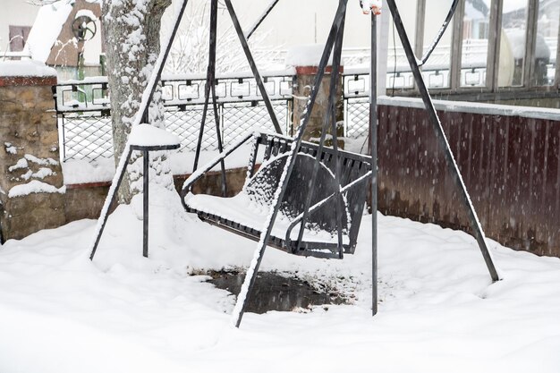 Swing covered with snow. Snow falls.