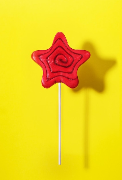 Swirl lollipop candy on a stick on yellow background, top view