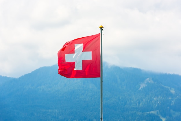 Swiss flag against Alps mountains. Horizontal shot