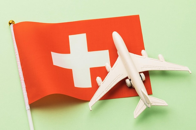 Swiss flag and toy plane on a colored background, concept of flight to Switzerland, top view