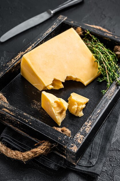 Swiss Hard cheese piece in wooden tray. Black background. Top view.