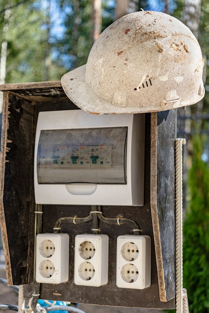 A switchboard on a construction site with sockets and an old work helmet hanging from it. Providing electricity to the construction site.