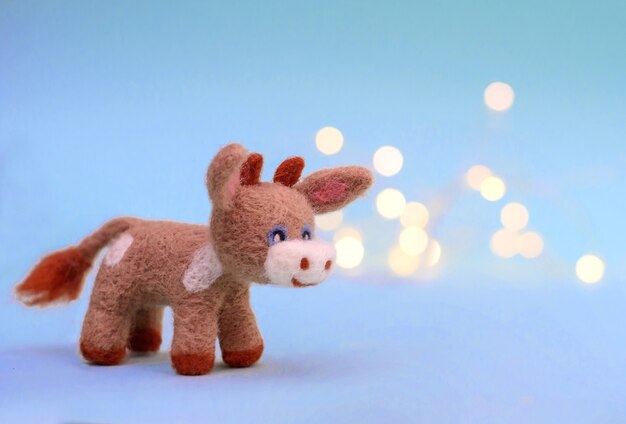 Symbol of 2021, a toy felt bull or cow on a festive light blue\
background with bokeh, with a copy space