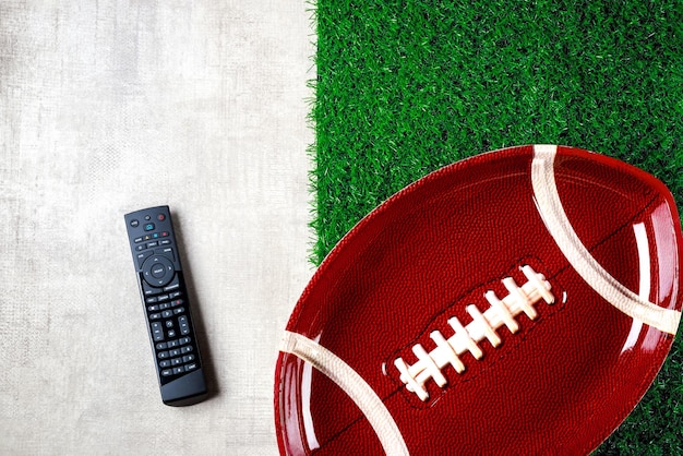 Symbol of american football ball plate with remote controller\
on white and green background. mockup, copy space.