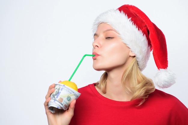 Symbol of wealth and richness. Christmas lemonade punch. Girl santa hat drink juice lemon wrapped in banknote. Totally natural lemonade. Girl with lemonade and money. Fresh lemonade drink with straw.