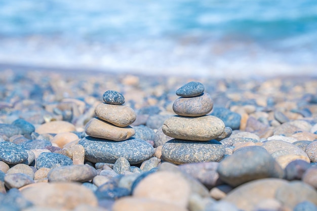 Symbolic scales of stones against the background of the sea and blue sky Concept of harmony and balance Pros and cons concept Pyramid stones balance on the sand of the beach with blurred background