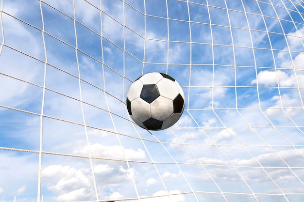 Symbolic of success and victory classic soccer ball football have black and white color going into ingoal net after shooted in the game with a blue sky background success concept