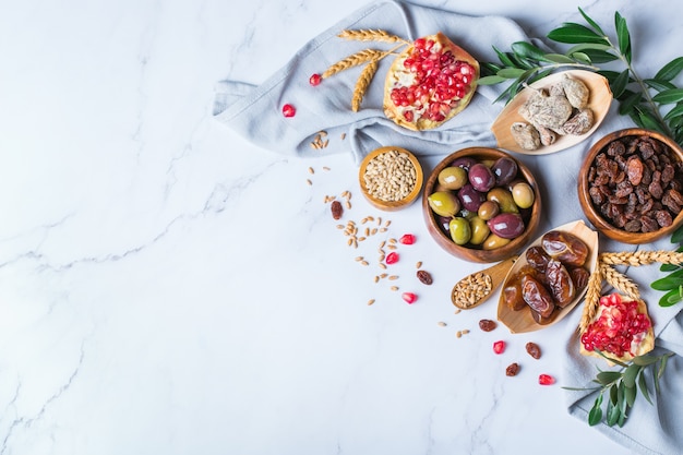 유대교 휴일 Tu Bishvat, 나무의 Rosh Hashana 새해의 상징. 대리석 테이블에 말린 과일, 대추, 무화과, 포도, 보리, 밀, 올리브, 석류를 섞으세요. 공간 배경 복사