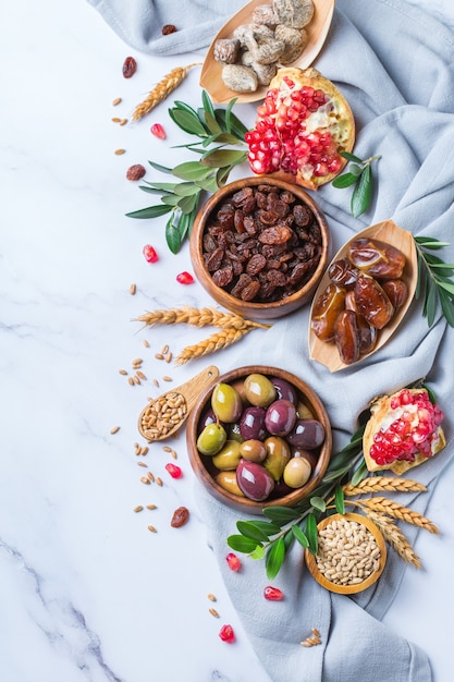 Symbols of judaic holiday Tu Bishvat, Rosh Hashana new year of the trees. Mix of dried fruits, date, fig, grape, barley, wheat, olive, pomegranate on a marble table. Copy space background