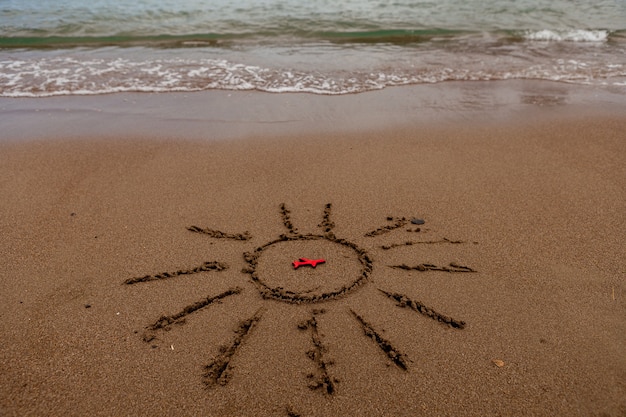 Symbool van de zon en een vliegtuig door de zee geschilderde zon op het zand zeekust figuur van een rood vliegtuig zee...