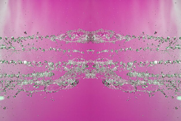 Symmetrical pattern of stopped water droplets with transparent streams on a pink background