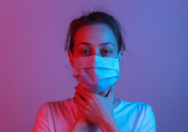 Symptoms of the flu. Woman in medical mask holds throat. Red blue neon gradient light