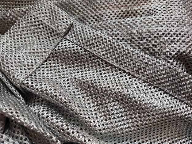 Синтетическая полиэфирная ткань с дырками Абстрактный фон Сложенный волной кусок ткани серого или серебристого цвета Аккуратно подшитая ткань