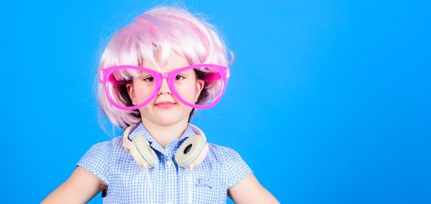 Synthetisch haar Cool klein kind met roze haarpruik Schattig klein meisje met mooie haarstijl met koptelefoon Schoonheidslook van gek haarmodel kopieerruimte