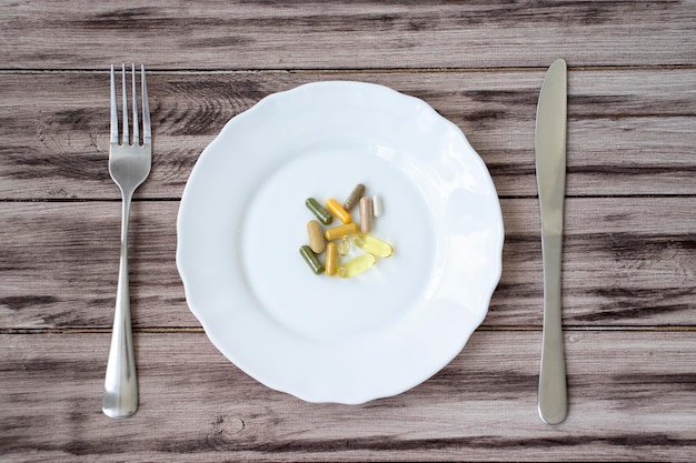 Synthetische vitamines en pillen op een bord met een mes en vork op een houten achtergrond