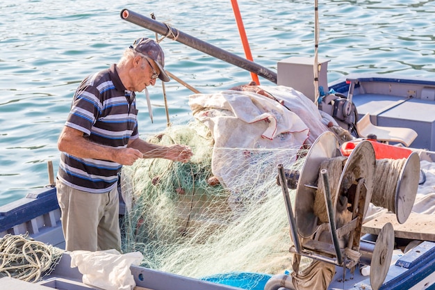 写真 シラキュース、イタリア：ボートでネットを解く上級漁師