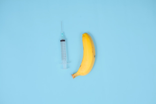 Siringa, banana e contraccezione isolati su sfondo blu
