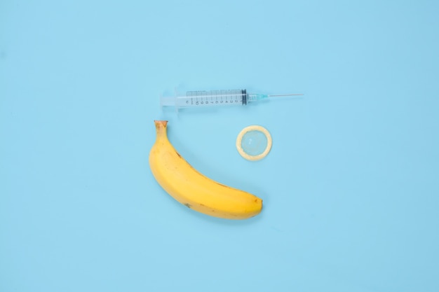 Foto siringa, banana e contraccezione isolati su sfondo blu