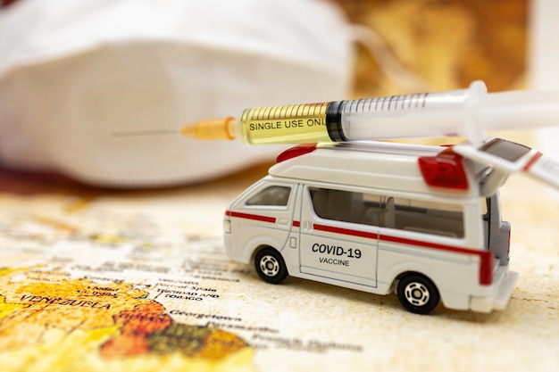 Syringe of COVID-19 vaccine on ambulance car with medical mask and world map background . Vaccine and Healthcare Medical concept.