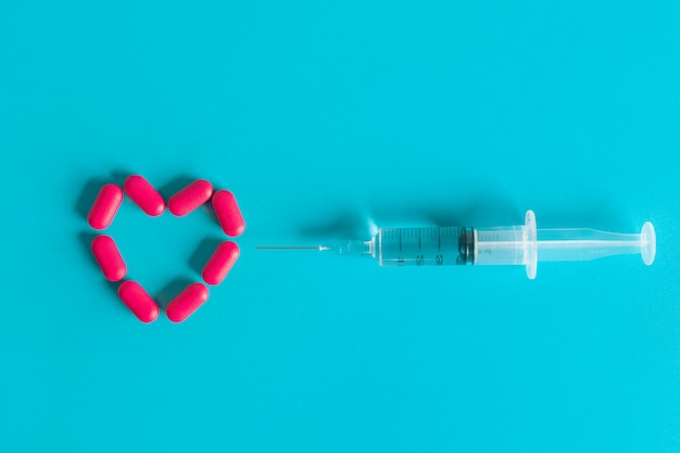 A syringe drawn by a medicinal product lies opposite a heart laid out of red pills. Health concept. 