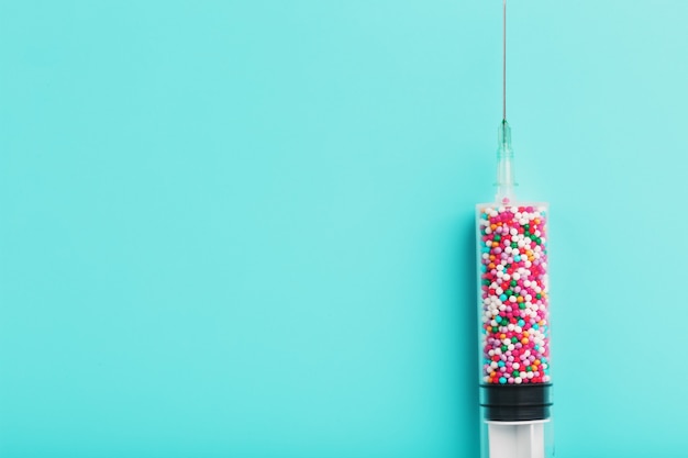 Syringe filled with colorful nano balls on a light blue