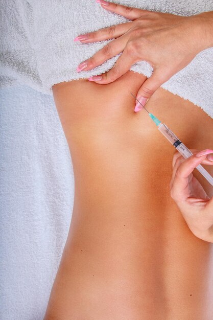 Syringe injection in to woman's back. Female enjoing relaxing back massage in cosmetology spa centre.