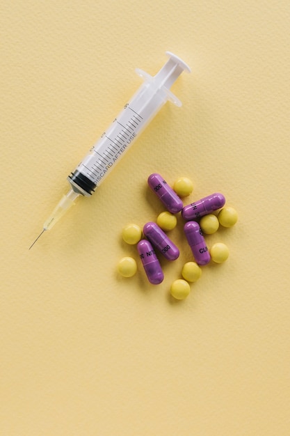 Syringe injector application device with needle and pills on yellow textured background