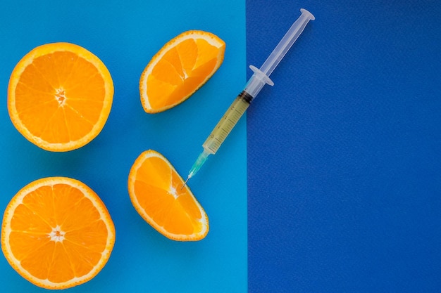 Syringe is ready for mesotherapy injection Orange in a Cut and Syringe With Vitamin C on blue background Vitamins Against Medicationsnatural anti aging cosmetics serum ampullas and syringe