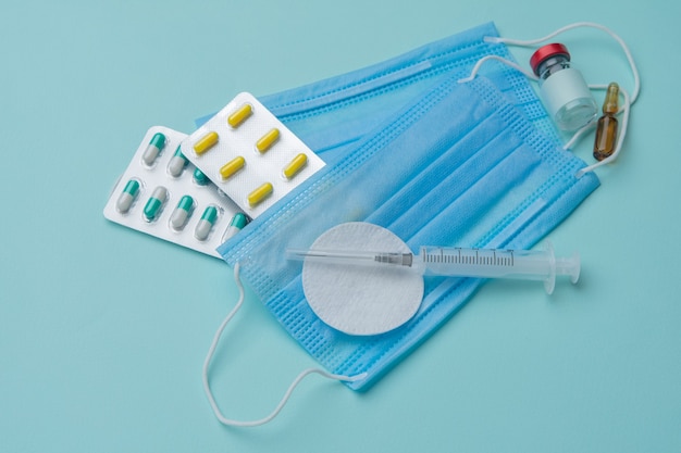 Syringe, mask, tablets, ampoules on a blue background, vaccination concept.