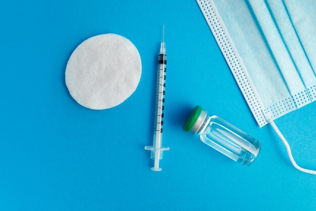 Syringe, medical mask and ampoule with medicine on a blue background