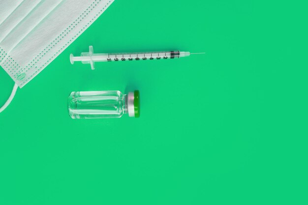 Photo syringe, medical mask and ampoule with medicine on a green background