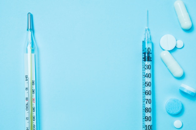 The syringe medicine and medical thermometer on pastel blue color