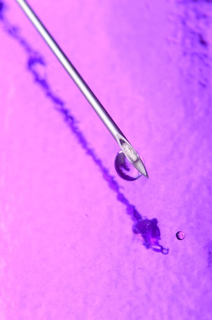 Syringe needle and a drop of a transparent substance closeup