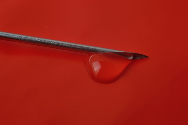 Syringe needle and a drop of a transparent substance closeup