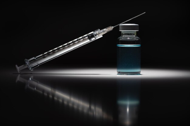 Syringe Needle and Medicine Vial With Light Blue Chemical Spot Lit on Reflective Background