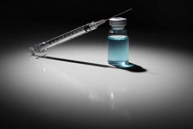 Photo syringe needle and medicine vial with light blue chemical spot lit on reflective background