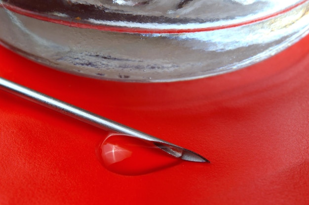 Syringe needle with a drop of a transparent substance and a glass jar closeup
