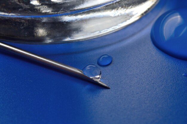 Syringe needle with a drop of a transparent substance and a glass jar closeup