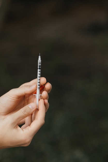 A syringe in a person's hand is held in front of a dark background.